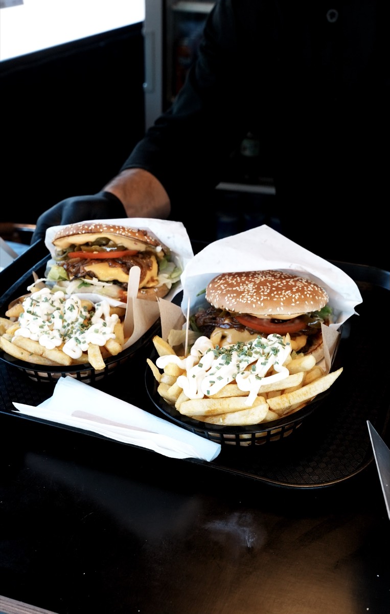 Zwei Tabletts mit Burgern und Loaded Fries werden über die Theke gereicht